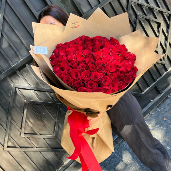 Large bouquet of red roses wrapped in brown paper with a red ribbon
