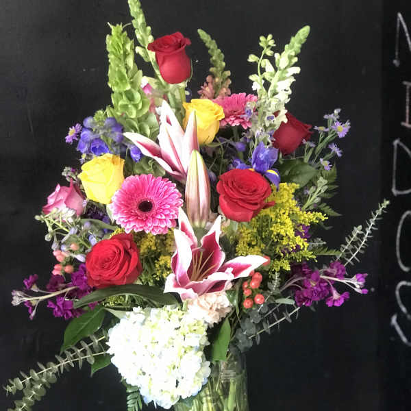 Mixed bouquet of roses, lilies, and gerbera daisies in a glass vase