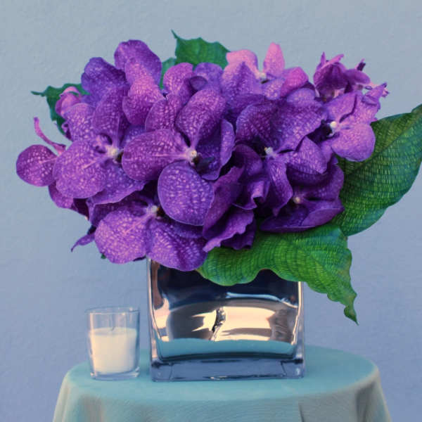 Purple orchid arrangement in a glass vase with a small candle beside it