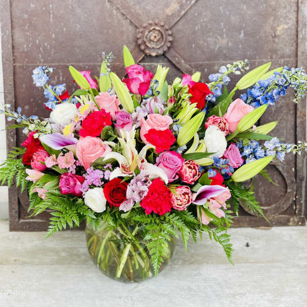 Mixed bouquet of pink, red, white, and blue flowers in a glass vase