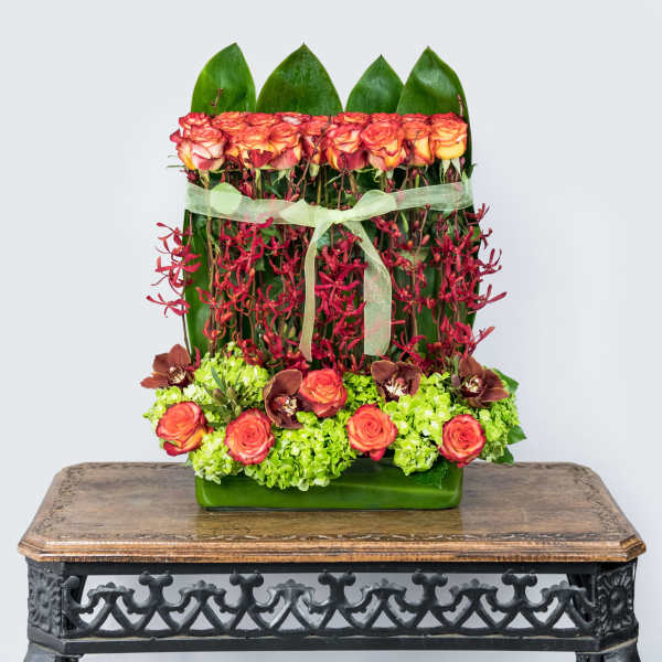Tropical floral arrangement with orange roses and red orchids in a green vase