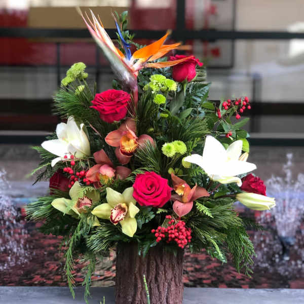 Tropical floral arrangement with roses, lilies, and orchids in a wood-look container
