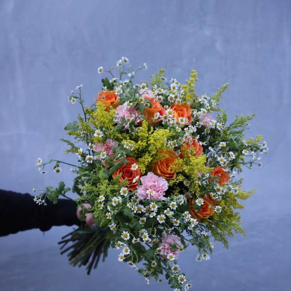 Handheld bouquet of orange and pink flowers with small white daisies