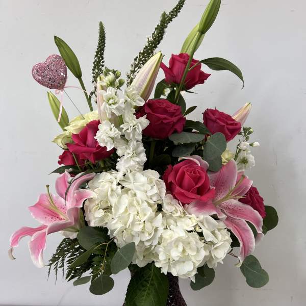 Pink roses and lilies arranged in a dark glass vase with white hydrangeas.
