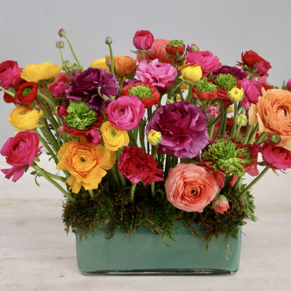 Low rectangular vase filled with bright pink, yellow, orange and green blooms in a dense arrangement