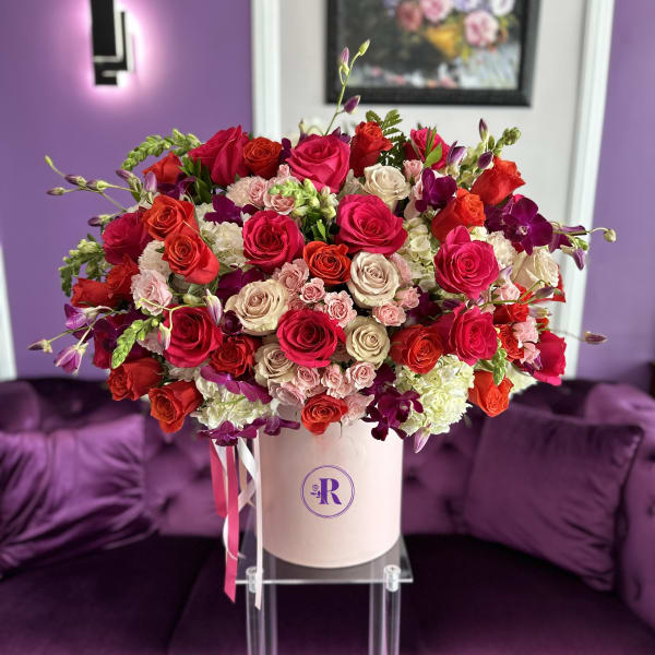Large hatbox arrangement of red, hot pink, and cream roses with orchids in a blush pink box.