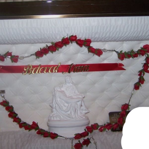 Red rose garland framing a white quilted casket interior with a crucifix