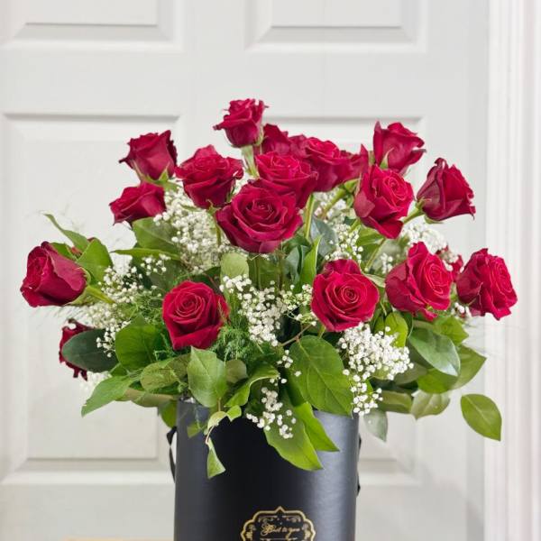 Red roses arranged in a black hat box with baby's breath