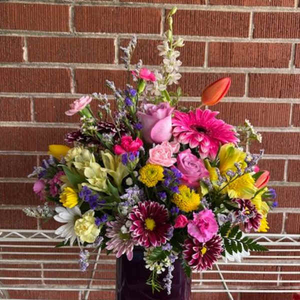 Mixed bouquet in a purple glass vase with pink, yellow, and white flowers