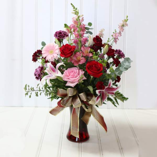 Mixed bouquet of roses, lilies, and pink blooms in a red glass vase