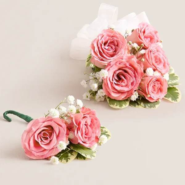 Two pink rose boutonnieres with white baby's breath and ribbon