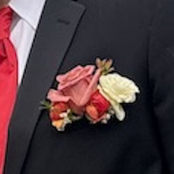 Pink, red, and cream rose boutonniere on a dark suit jacket