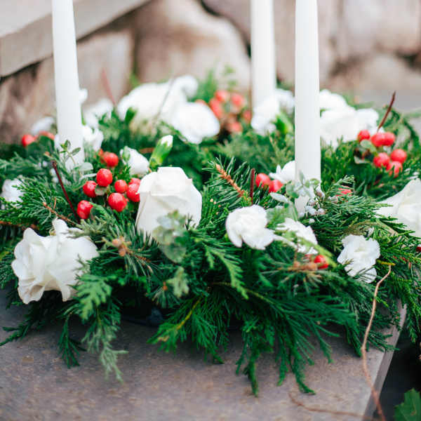 Evergreen candle ring with white flowers, red berries, and three white taper candles