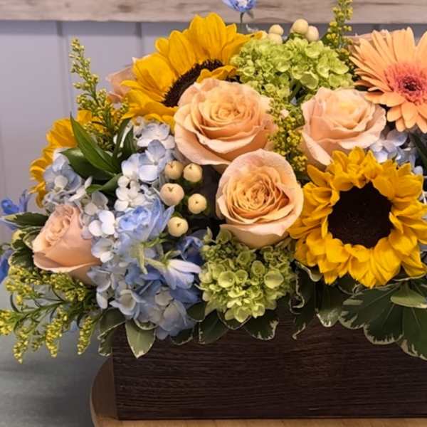 Mixed bouquet with sunflowers, peach roses, and blue hydrangeas in a wooden box