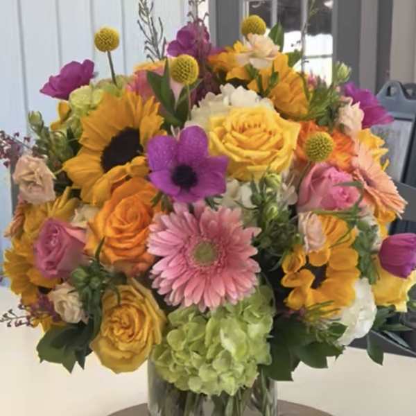 Colorful bouquet in a clear glass vase with roses, sunflowers, and gerbera daisies