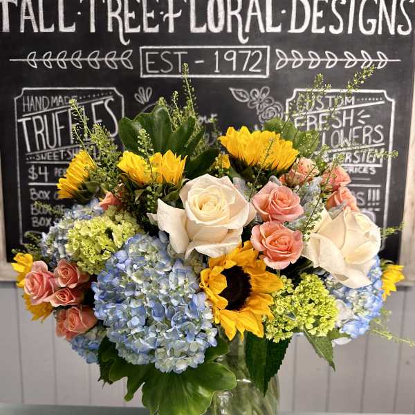 Mixed bouquet of sunflowers, roses, and hydrangeas in a glass vase