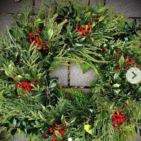Evergreen wreath with glossy foliage and clusters of red berries on a stone surface
