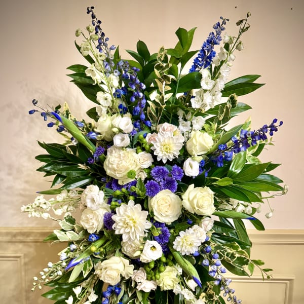Tall standing spray of white and purple flowers with blue accents on a metal easel