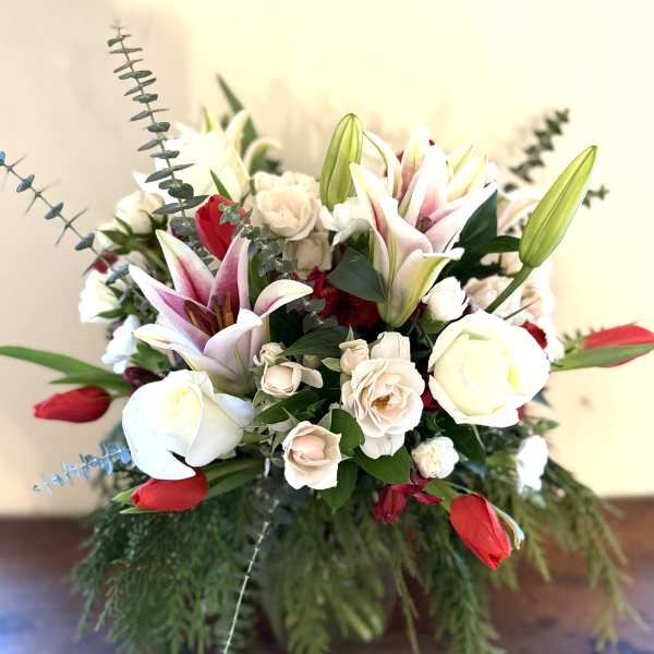 Arrangement of white roses, blush lilies, and red tulips in a clear vase with cascading greenery.
