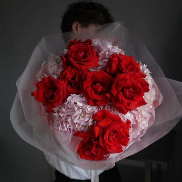Bouquet of red roses and pale pink flowers wrapped in sheer paper