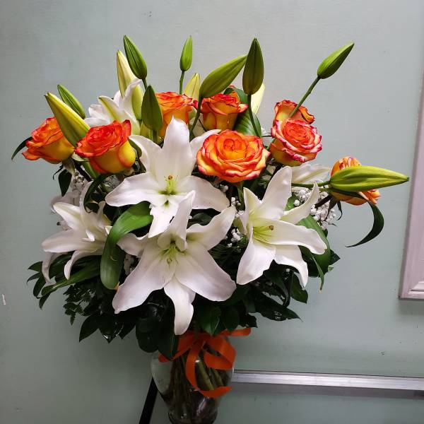 Bouquet of white lilies and orange roses in a glass vase