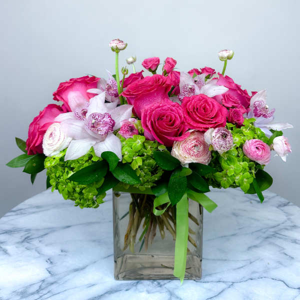 Pink roses and white orchids in a clear square vase