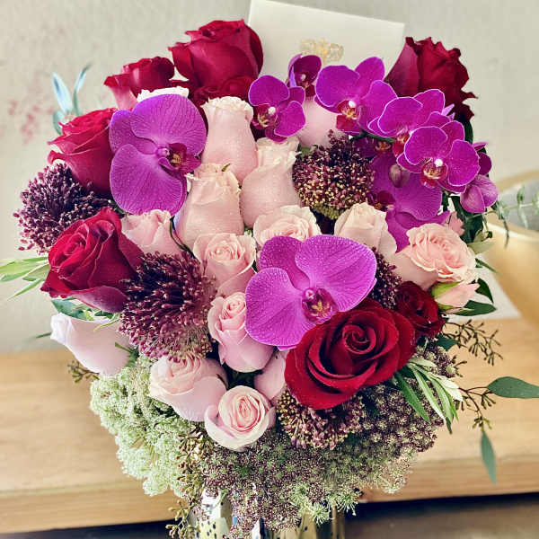 Bouquet of red and pink roses with purple orchids in a gold vase