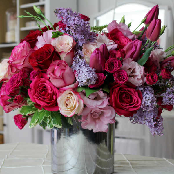 Bouquet of pink and red roses with purple lilacs in a silver vase