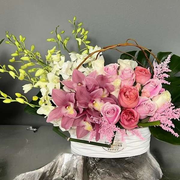 Pink roses and orchids arranged in a white basket with large green leaves