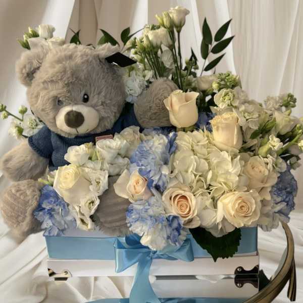 Teddy bear in a box with white and blue flowers