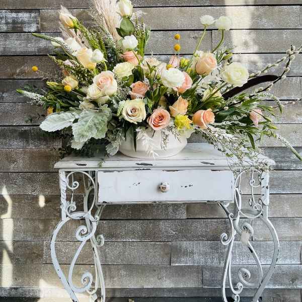 Large pastel floral arrangement in a white bowl on a decorative table