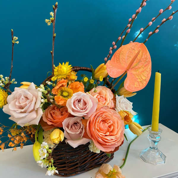 Basket arrangement of peach and pink roses with yellow accents and a candle