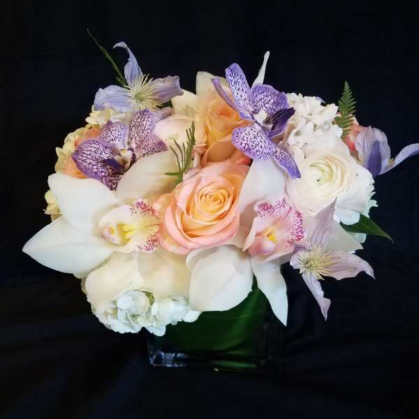 Pastel bouquet of roses, orchids, and white lilies in a glass vase