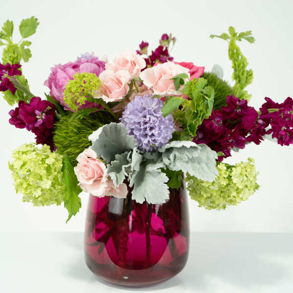 Mixed bouquet in a magenta glass vase with pink, purple, and green blooms