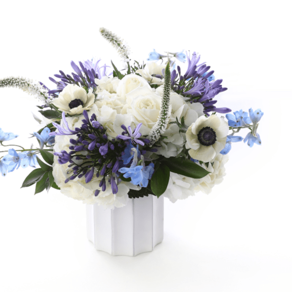White and purple floral arrangement in a white vase with blue accents