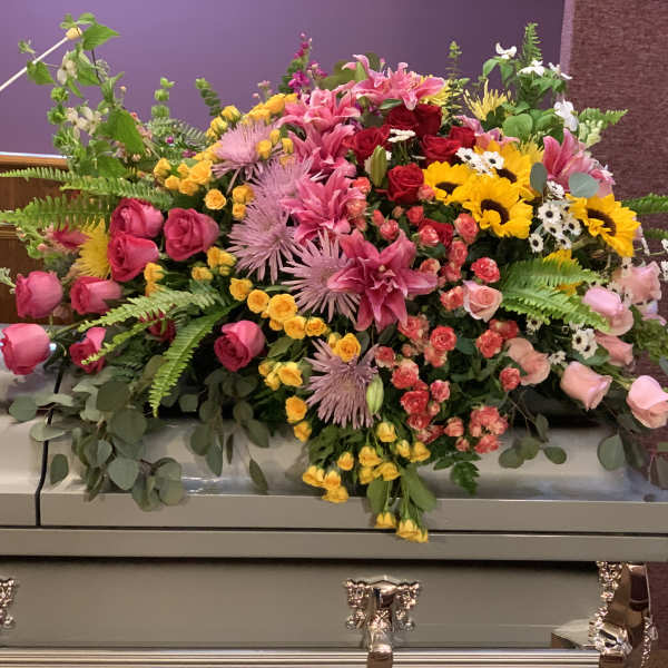 Large mixed floral spray on a casket with pink, yellow, and red blooms
