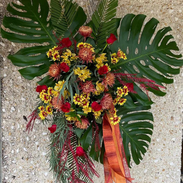 Tropical floral standing spray with red and yellow blooms and large palm leaves