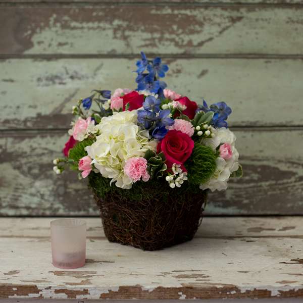 Mixed bouquet in a woven basket with roses, hydrangeas, and blue flowers
