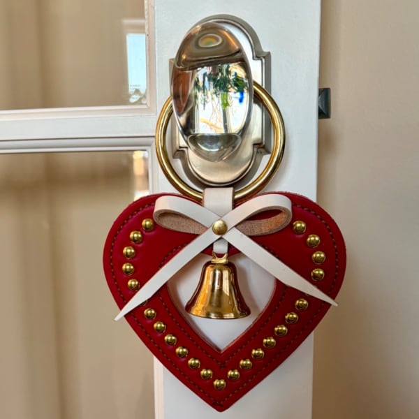 Red heart-shaped door hanger with a white bow and brass bell