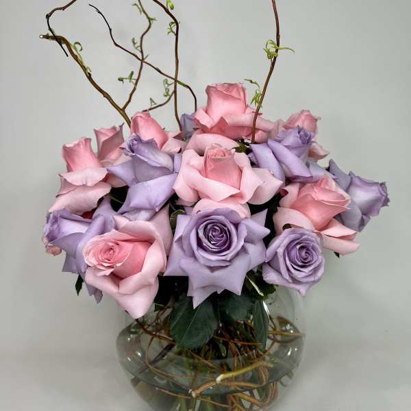 Pink and lavender roses arranged in a round glass vase with curly branches