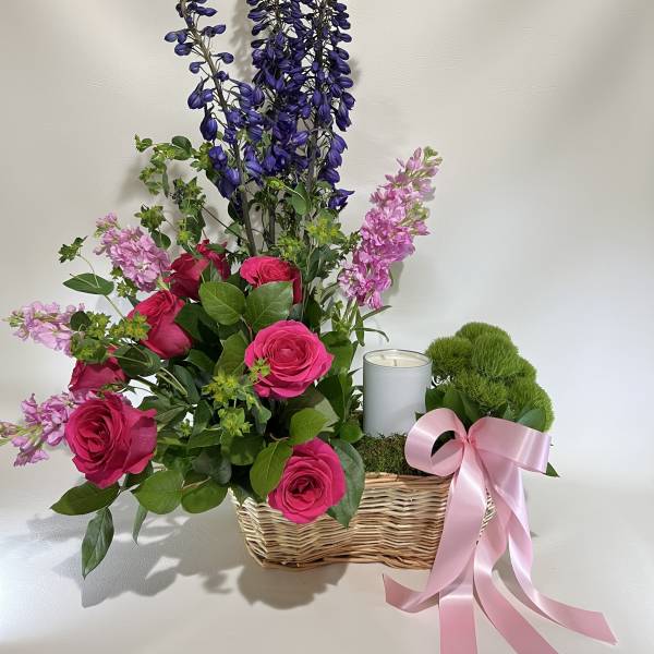 Pink roses and purple flowers in a wicker basket with a candle and pink ribbon