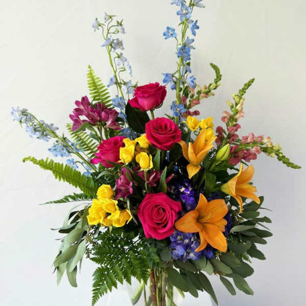 Colorful mixed bouquet of roses, lilies, and blue flowers in a glass vase