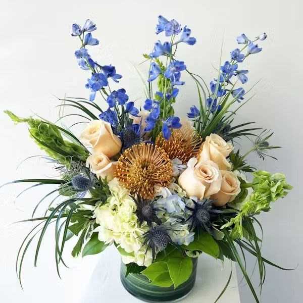 Mixed bouquet of blue, cream, and gold flowers in a glass vase