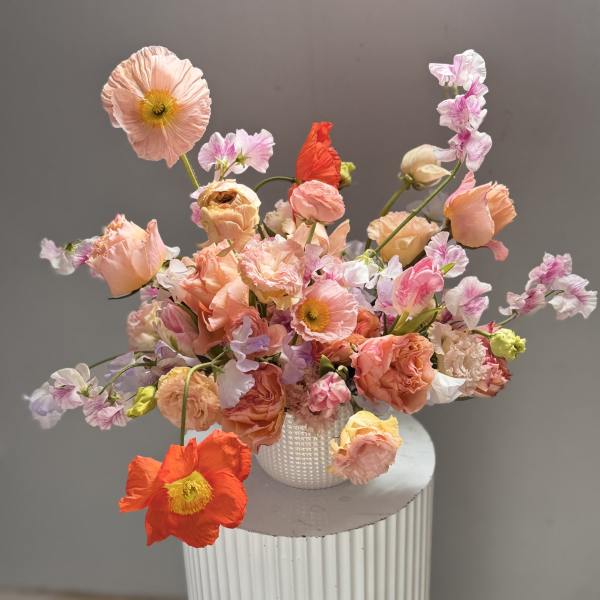 Loose bouquet of peach, pink, and coral flowers in a white vase