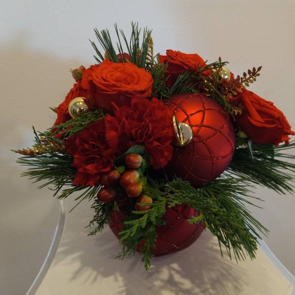 Red roses and carnations arranged with holiday ornaments in a vase