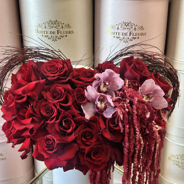 Heart-shaped box of red roses with pink orchids and trailing amaranthus
