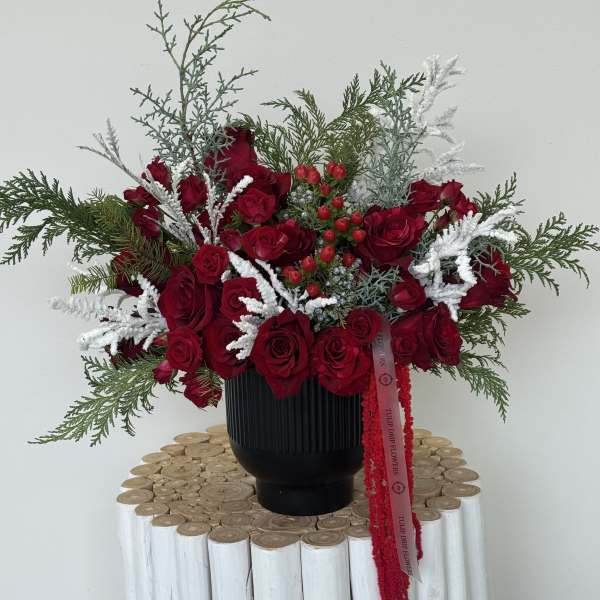 Red rose arrangement in a black vase with white frosted accents
