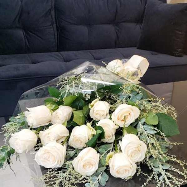 Hand-tied bouquet of white roses wrapped in clear cellophane on a black table