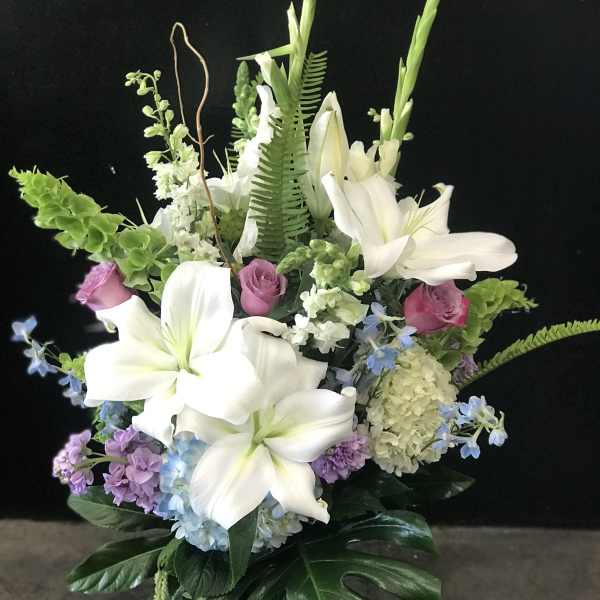 White lilies and pastel flowers arranged in a glass vase
