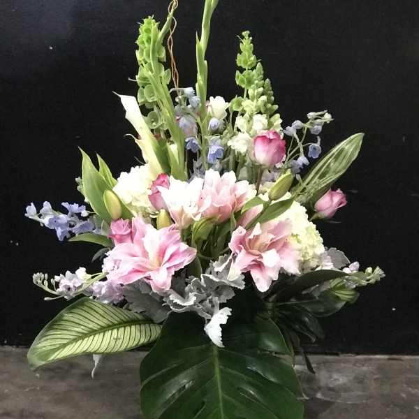 Tall bouquet of pink lilies, white callas, and blue flowers with large tropical leaves